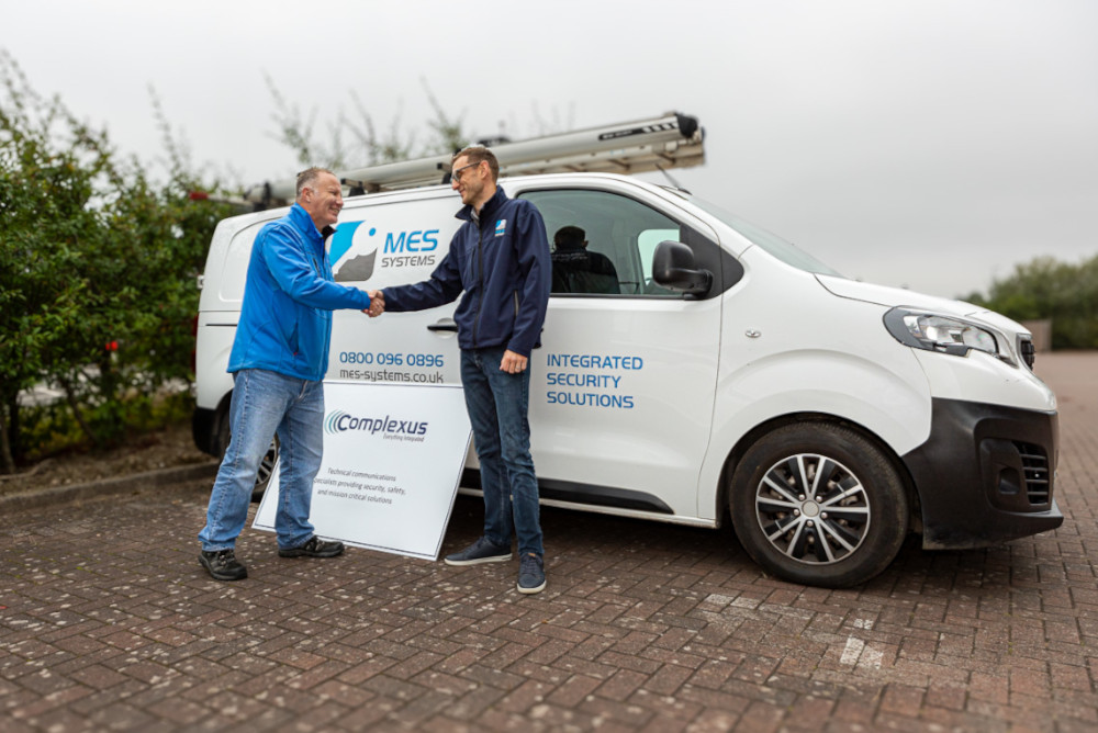 Complexus Director and client MES Systems shaking hands in front of van with a tracking device